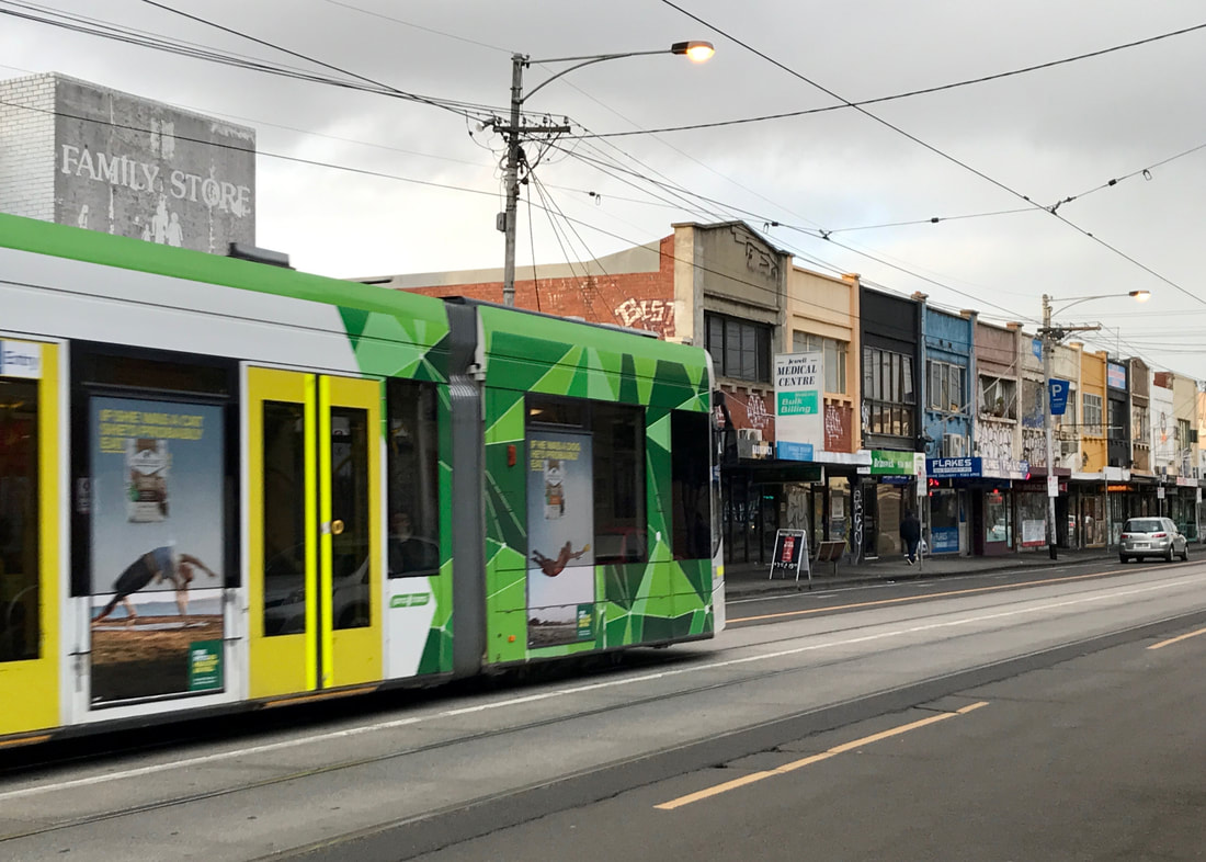 Streetscape showing green and yellow tram and a line of two story buildings with shop fronts along the bottom story