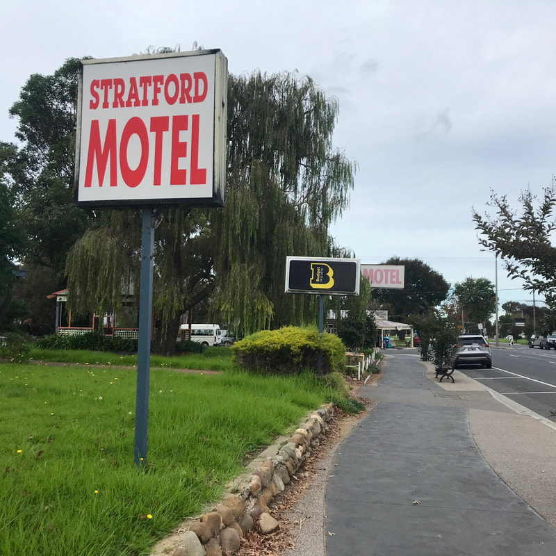 Streetscape with three large signs reading STRATFORD MOTEL and BUDGET HOTEL and MOTEL