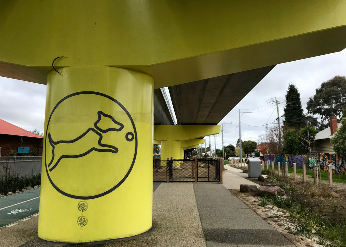 large piles painted bright yellow, one with a stylised image of a dog chasing a ball, indicating the dog park just beyond.
