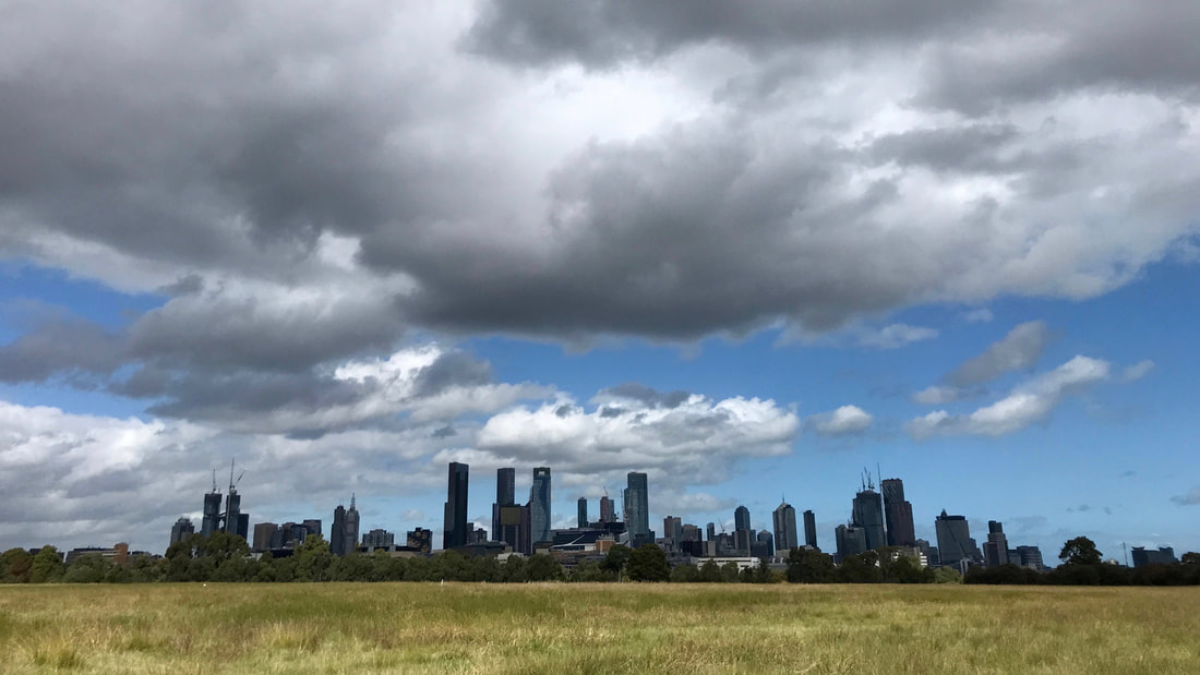 City skyline under a blue and cloudy sky, viewed from over an expanse of grass
