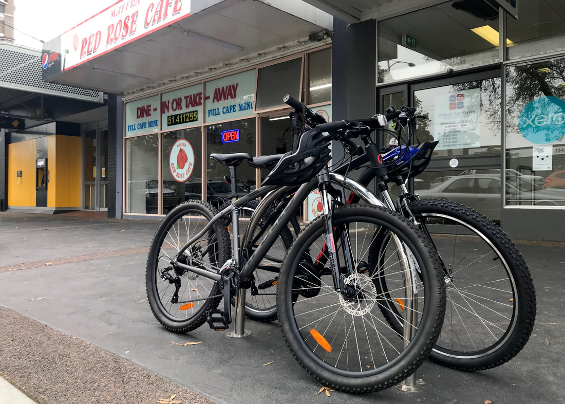 Two bikes on a bike rack and, in the background, the front of a takeaway shop