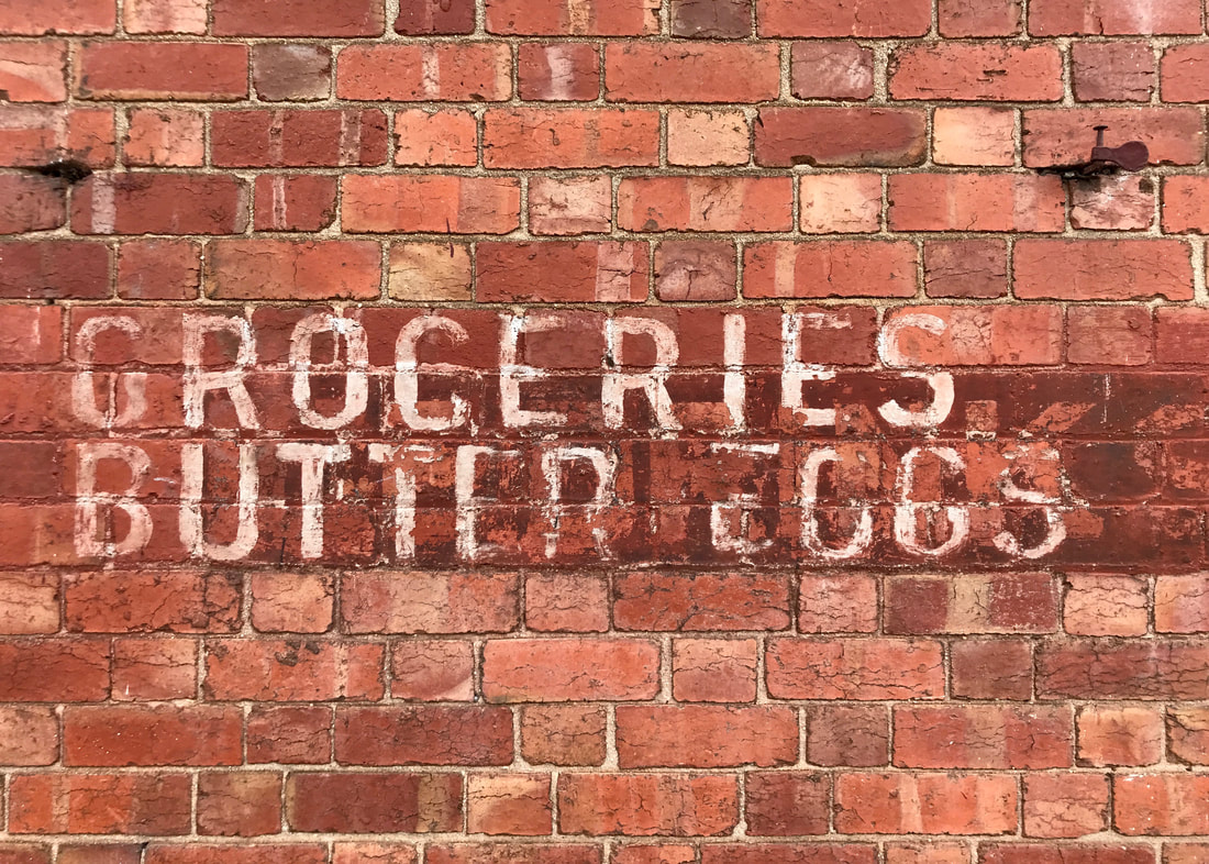 Brick wall with the following painted in fading white: GROCERIES BUTTER EGGS