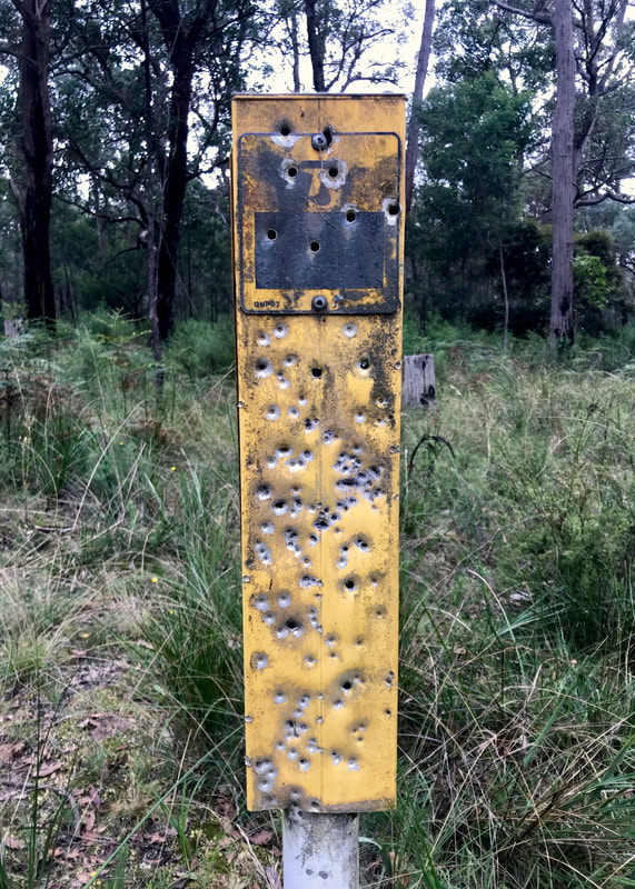 Yellow telstra sign covered in pellet holes from a shot gun