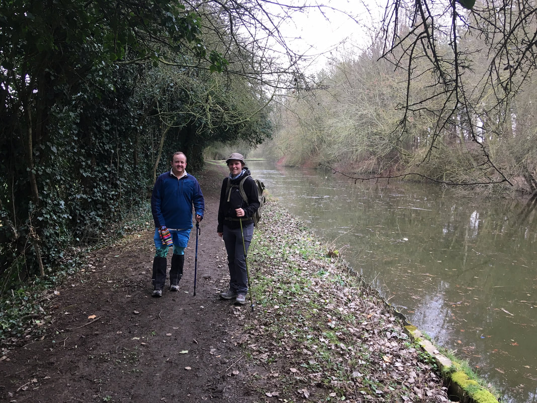 Two people stand on a slightly muddy path beside a canal
