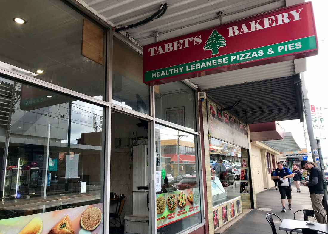Street scene with a sign for Tabet's Bakery, healthy lebanese pizzas & pies