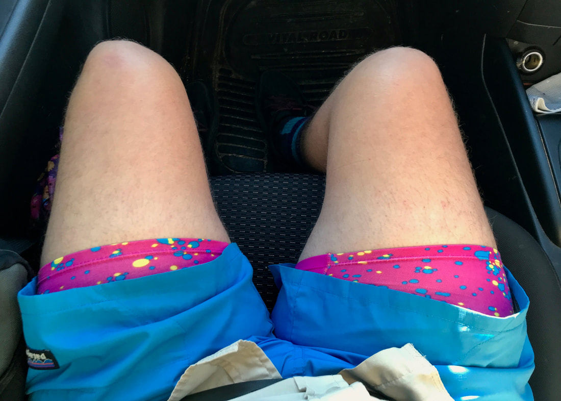 POV shot of legs sitting in a car, hot pink undies poking out the bottom of the legs of blue shorts