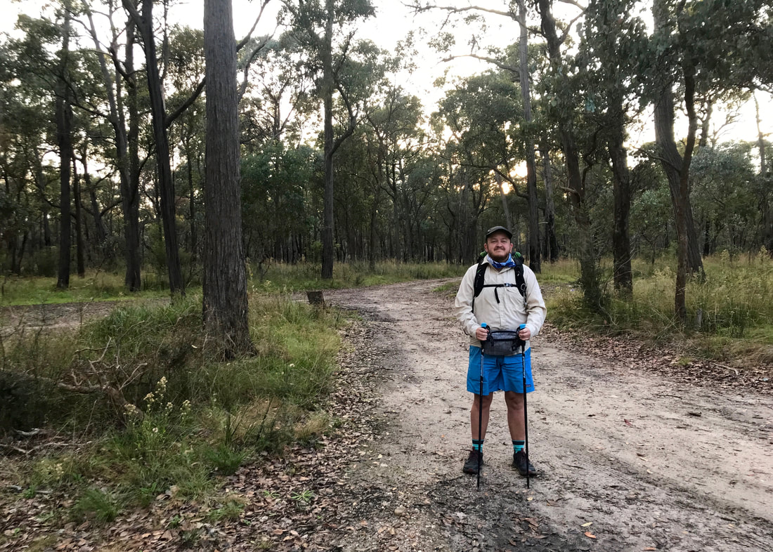 Person in backpacking gear - pack and walking poles - standing on a grey sandy road in the bush