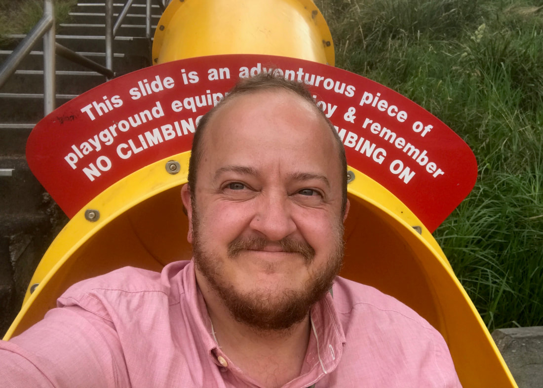 Selfie of a smiling person at the bottom of a yellow tubular slide