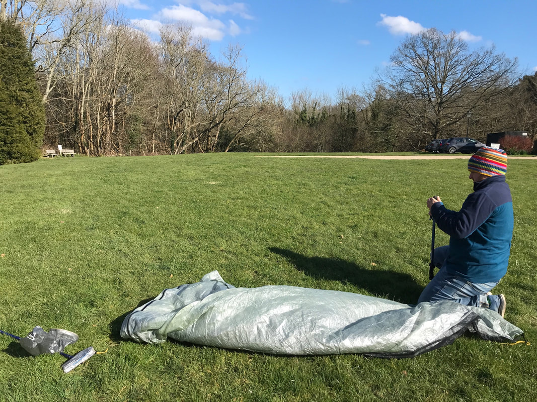 Person kneeling on grass with tent unrolled in front