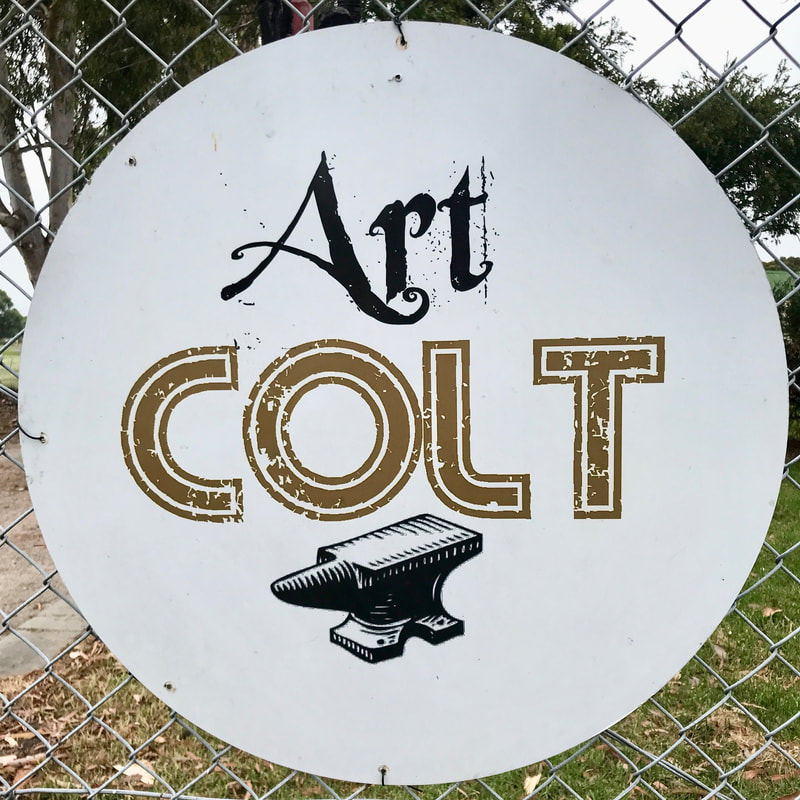 Round sign on a fence saying Art Colt with a picture of an anvil