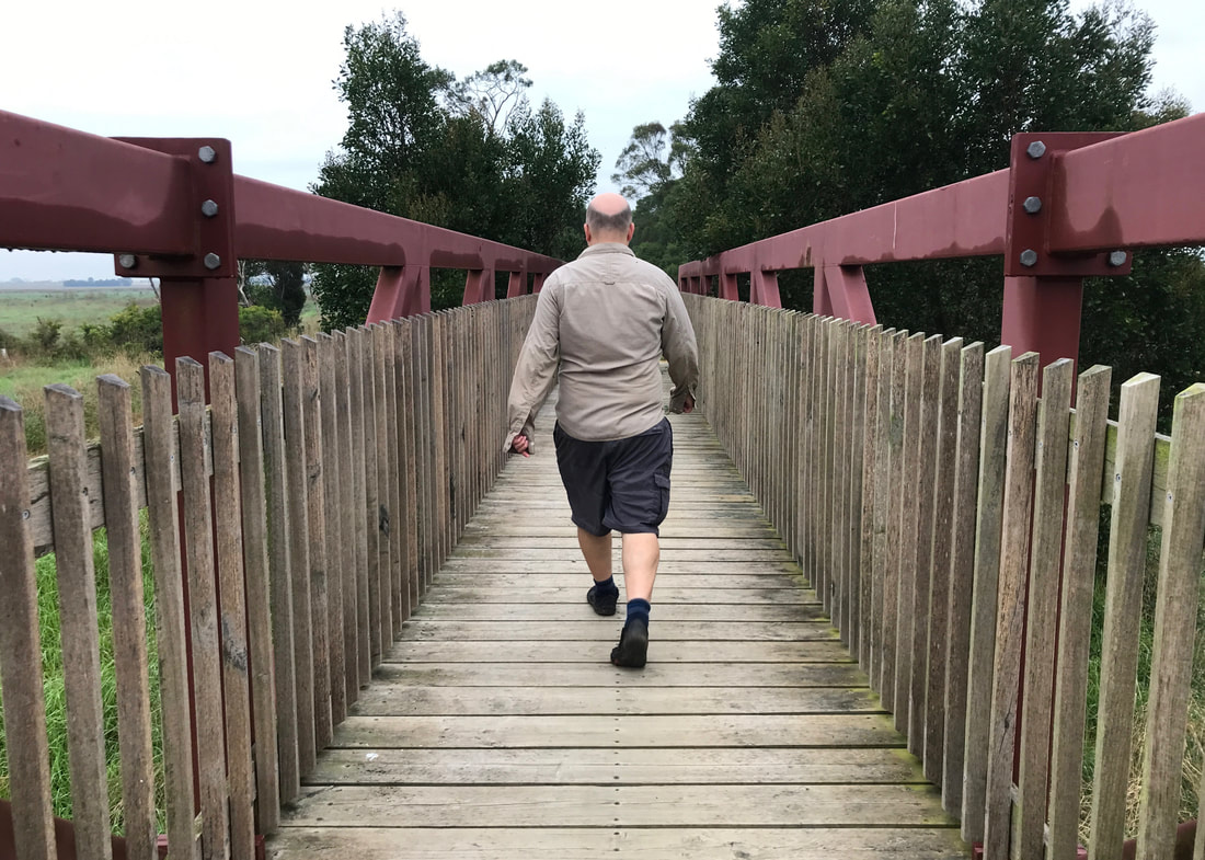 Person walking away from the camera on a wooden bridge with a dark red steel frame