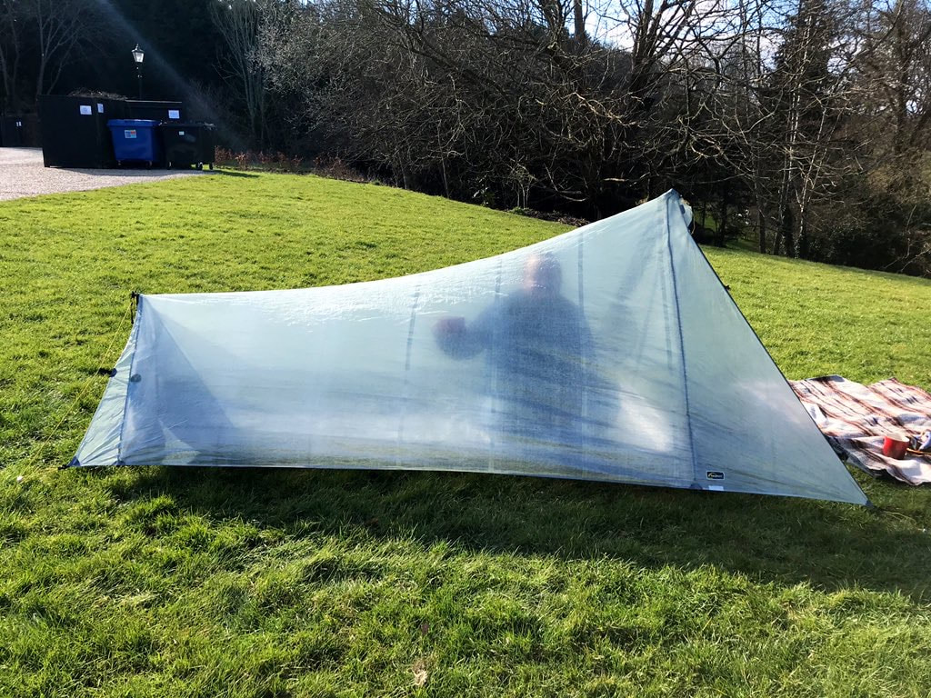 Tent set up on a sloping lawn. You can make out a person inside it.