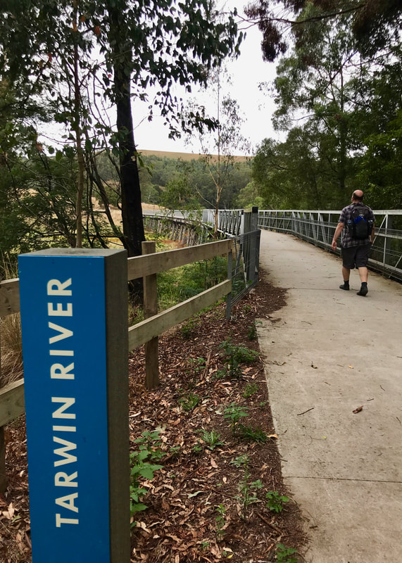 Person walking onto a long bridge, with a sign saying TARWIN RIVER in the foreground
