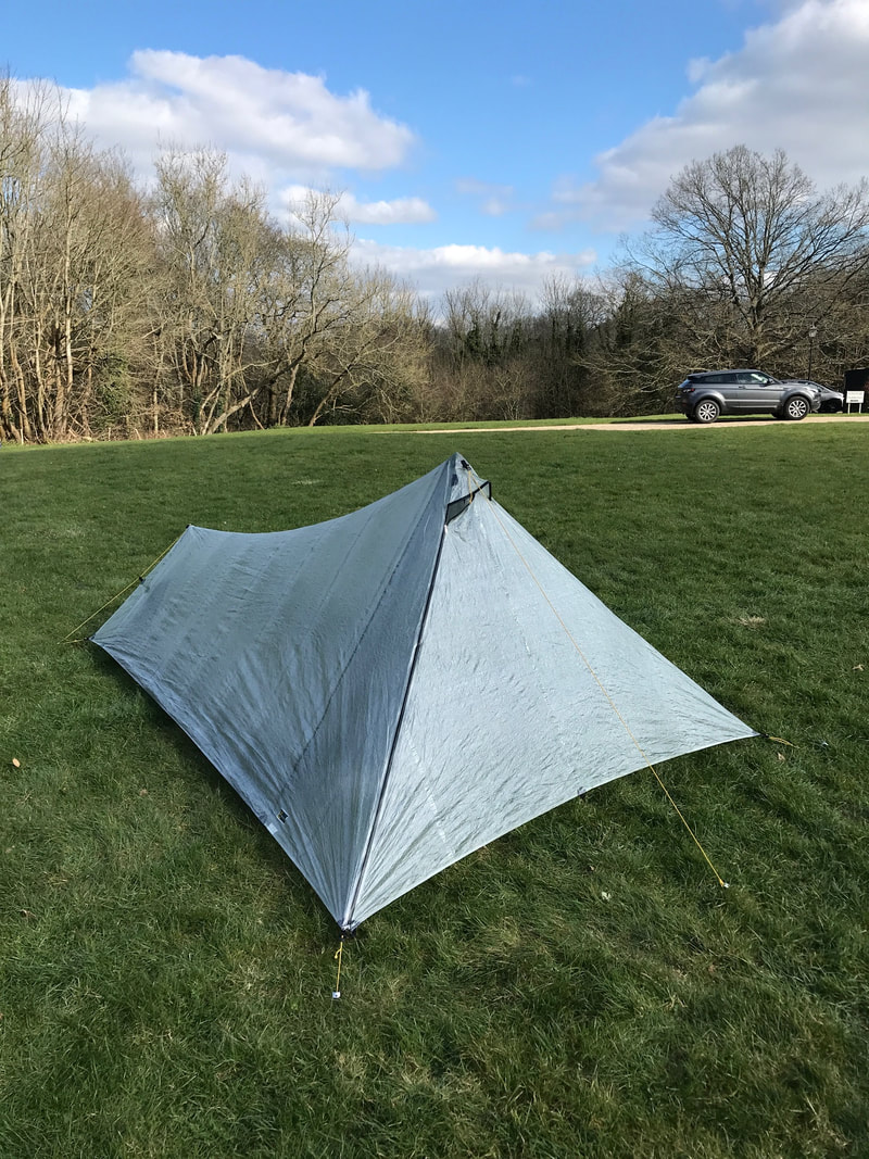 Tent pitched on expanse of grass with winter trees behind