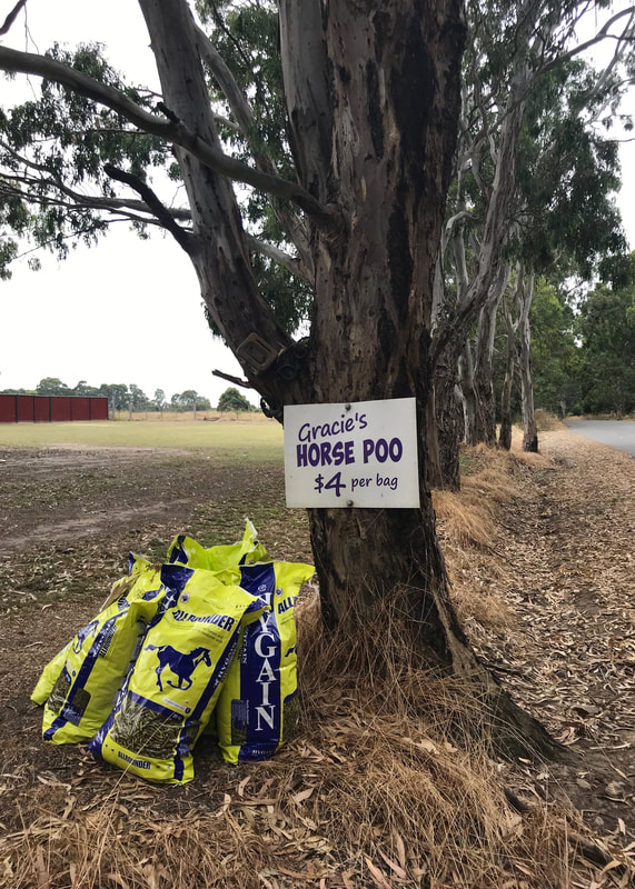 Bags of horse manure beside a tree, with a sign saying 