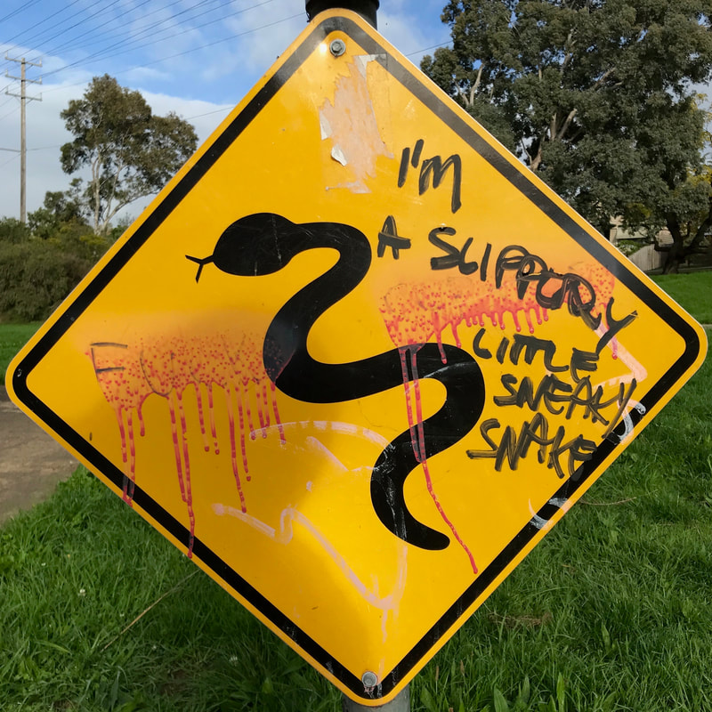 Yellow warning sign with snake silhouette, where someone has written on saying I'M A SLIPPERY LITTLE SNEAKY SNAKE