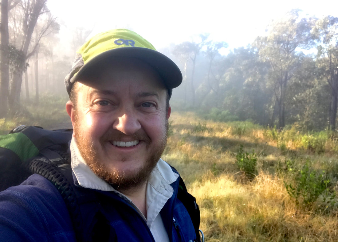 Selfie of smiling person in yellow cap, with slightly misty landscape behind
