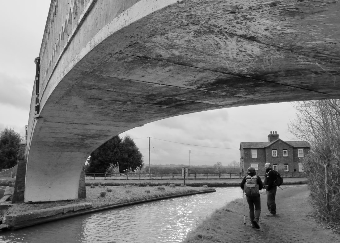 Bridge arch from beneath dominates image of two people walking
