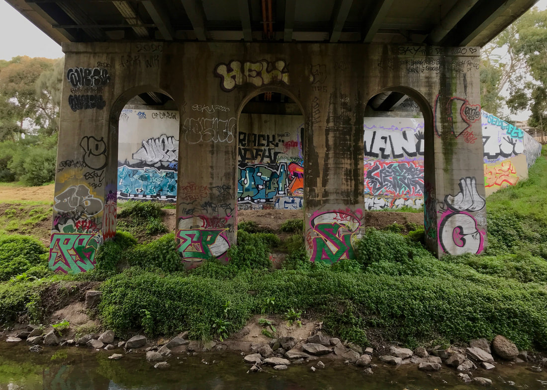 Concrete bridge with three arches covered in bright graffiti