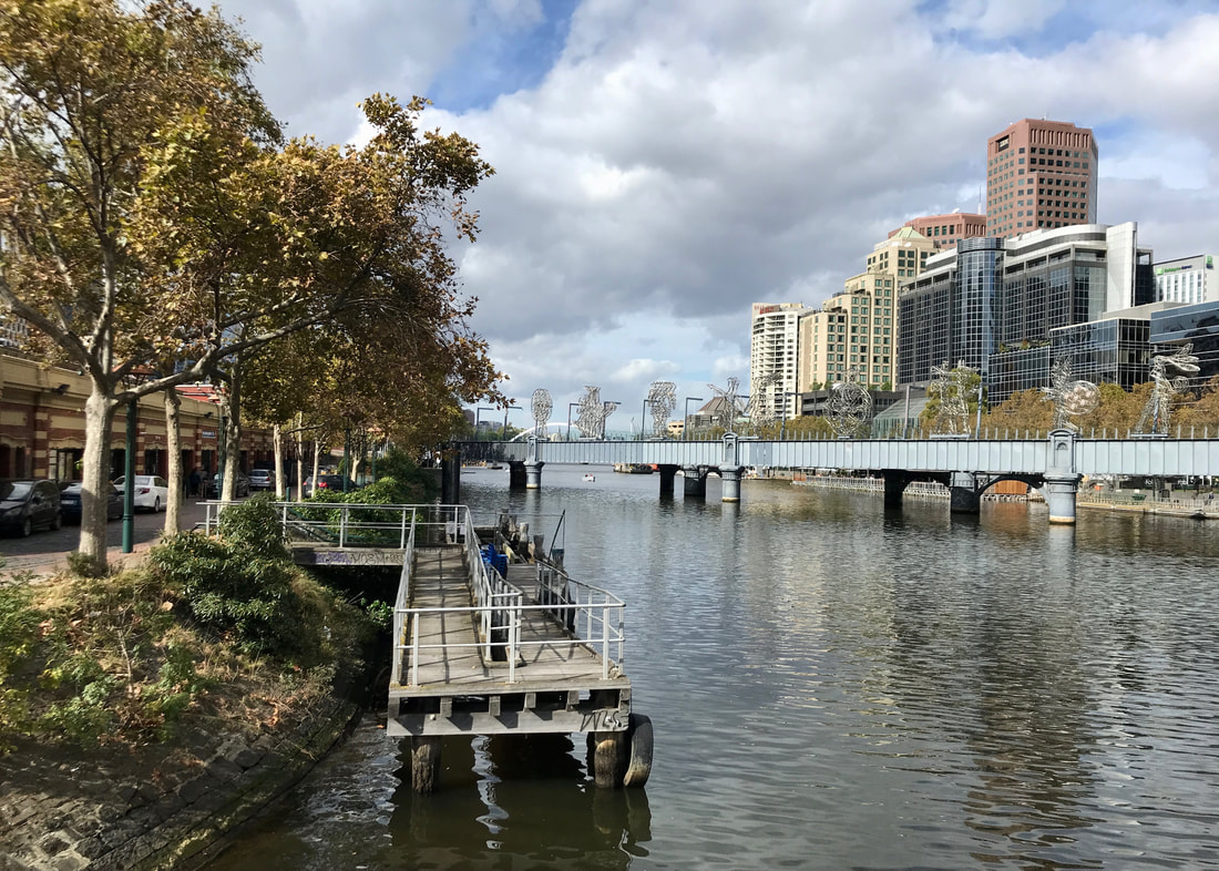 View up a river showing autumn trees, tall buildings and a bridge with many wiry scupltures
