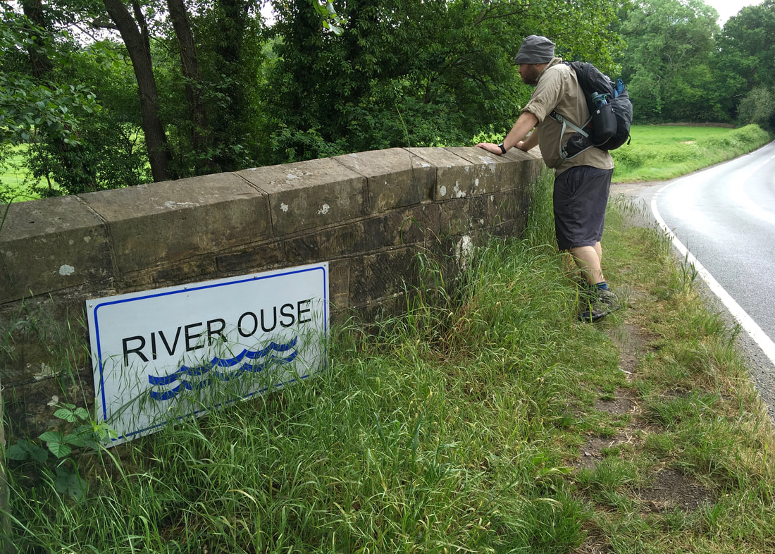 person looks over a stone bridge wall with a River Ouse sign