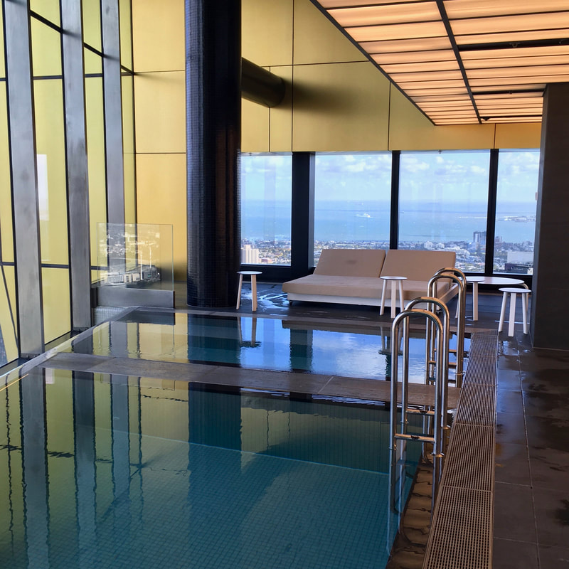 Small infinity pools and a poolside couch, with a view out the window to the edge of the city and the bay