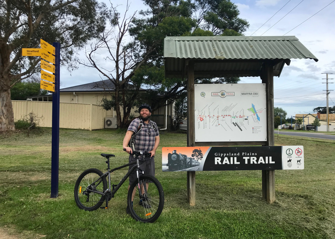 Person standing beside an information board and a fingerpost, holding a mountain bike and smiling