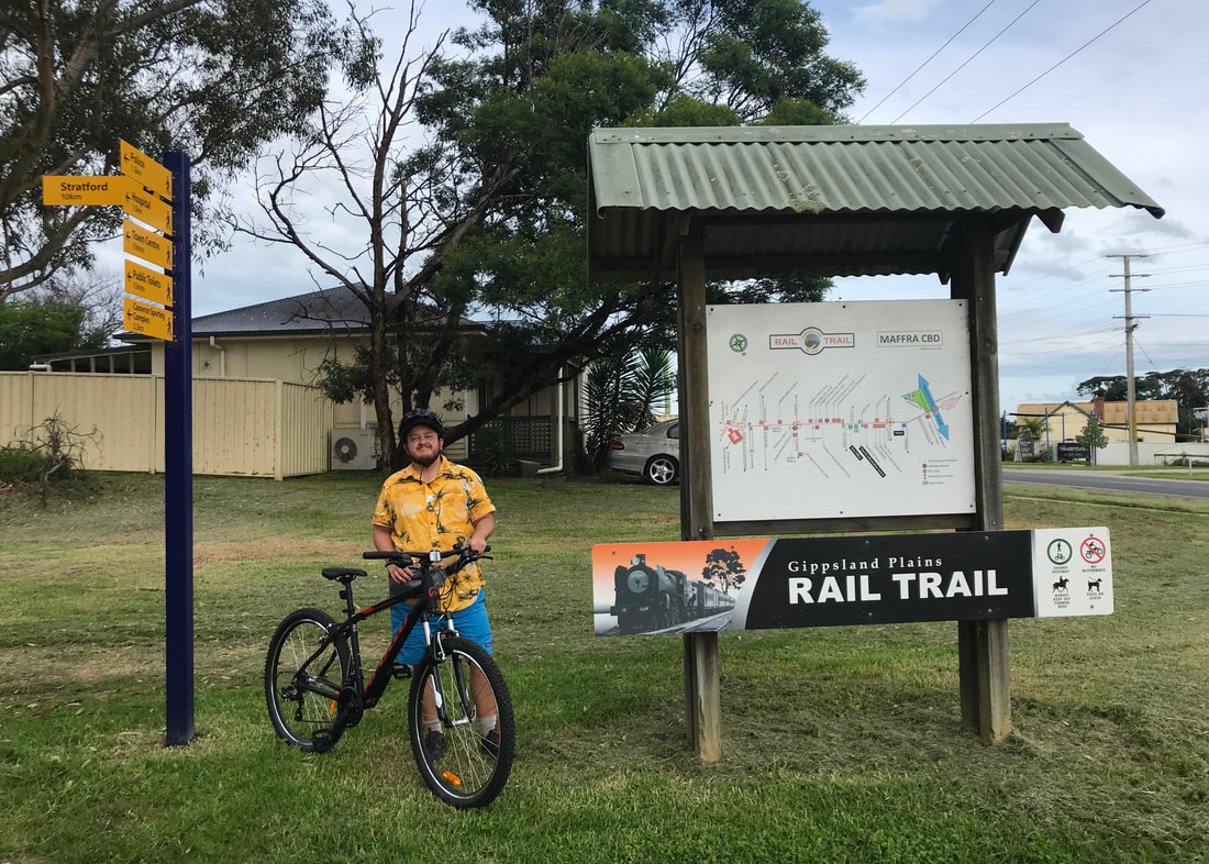 Person standing beside an information board and a fingerpost, holding a mountain bike and smiling