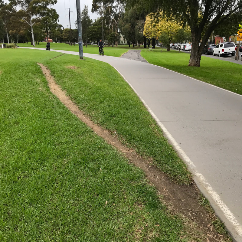 Concrete path curves right and left, as a narrow but clearly defined dirt path curves left and right over a small grassy rise
