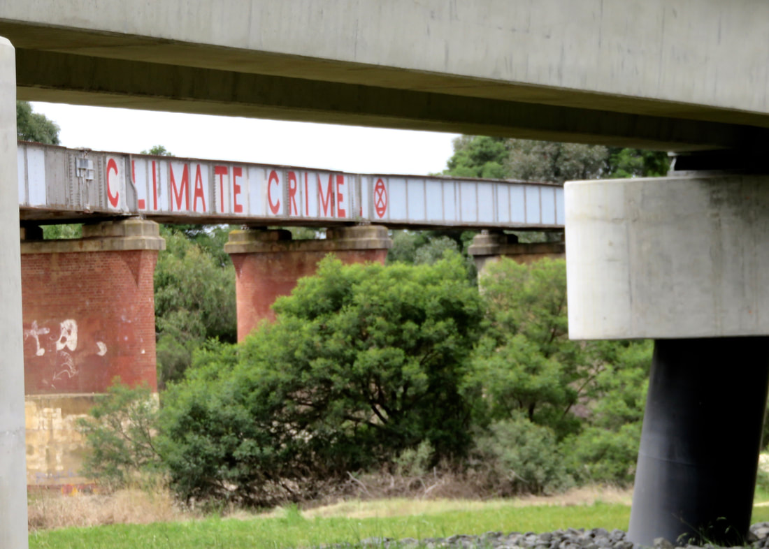 Framed by new concrete, the old bridge has brick pillars and CLIMATE CRIME graffitied in red along it