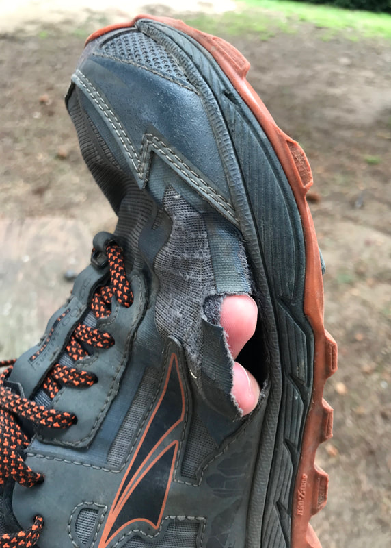 Grey and orange shoe, with a couple of fingertips poking out a hole in the side