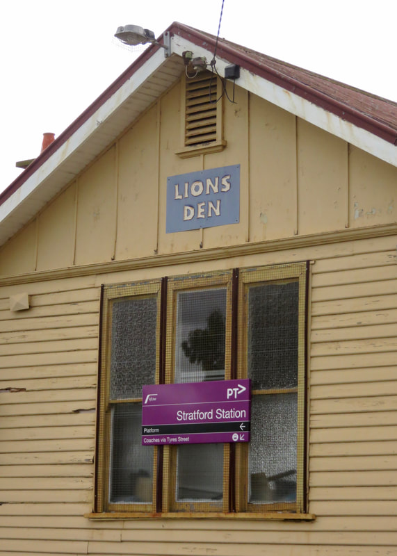 Dull yellow building with a new sign for Stratford Station and an old sign saying LIONS DEN