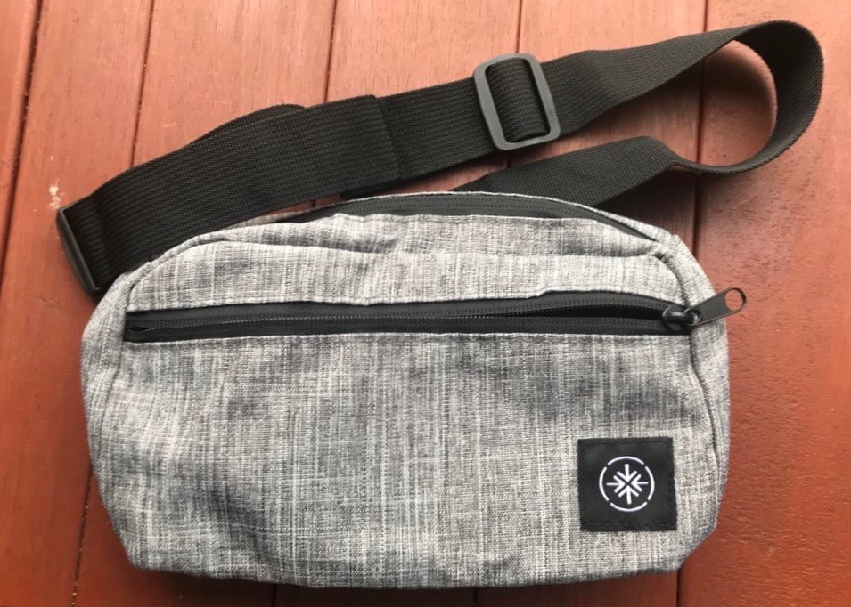 Grey bum bag or fanny pack with a black strap resting on a wooden table