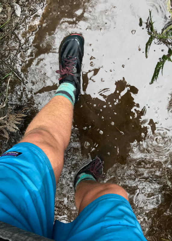 POV shot of legs and feet walking through shallow, muddy water
