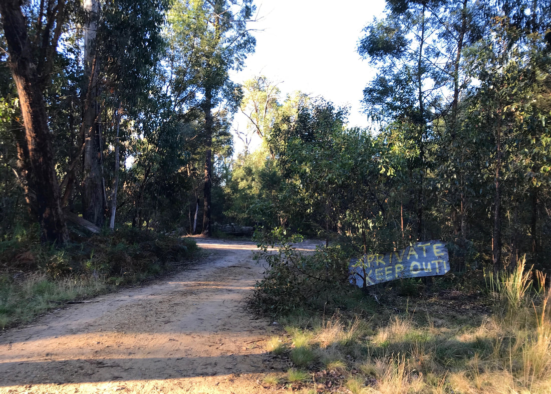 Dirt road with a handpainted sign on a piece of corrugated tin: PRIVATE KEEP OUT!