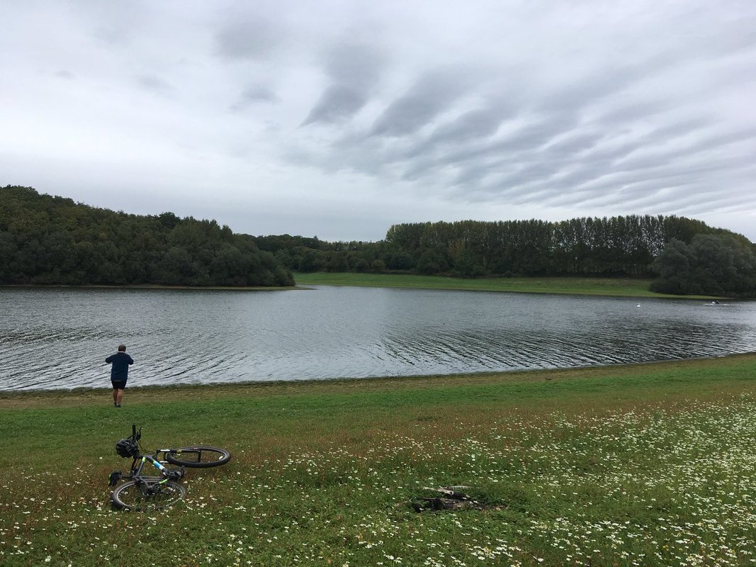 Person and bikes by water with cloudy sky