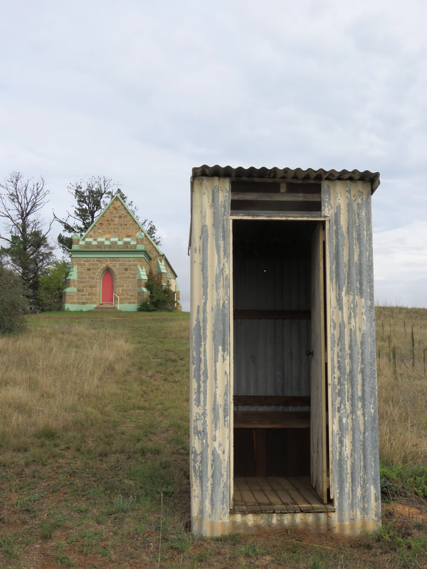 small, colourfully painted stone church, corrugated iron outdoors dunny
