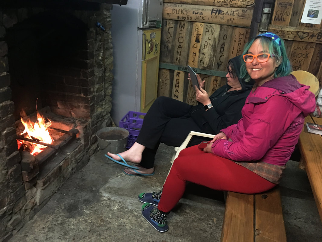 Two people sit in front of an open wood fire