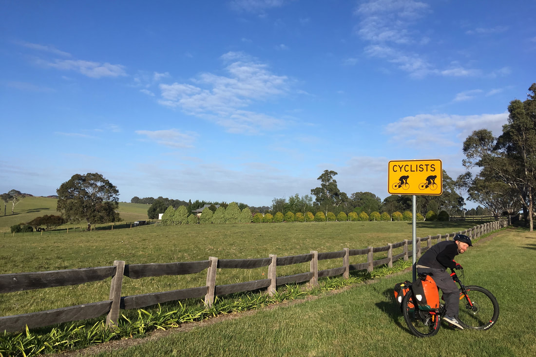 Landscape with pasture and trees, a person on a bike under a sign warning for cyclists