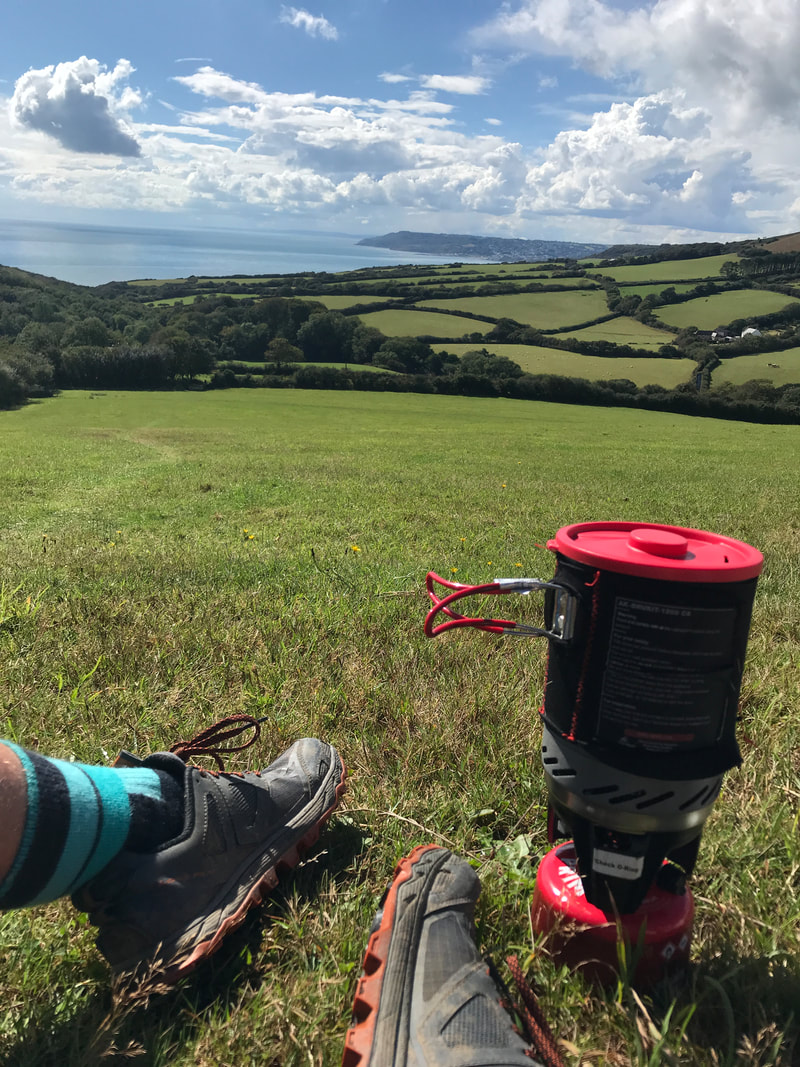 Green fields and coast seen over shoes and gas camping pot