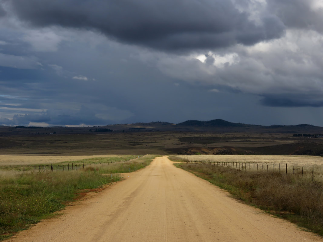 gravel road leading to distant hills and dark clouds