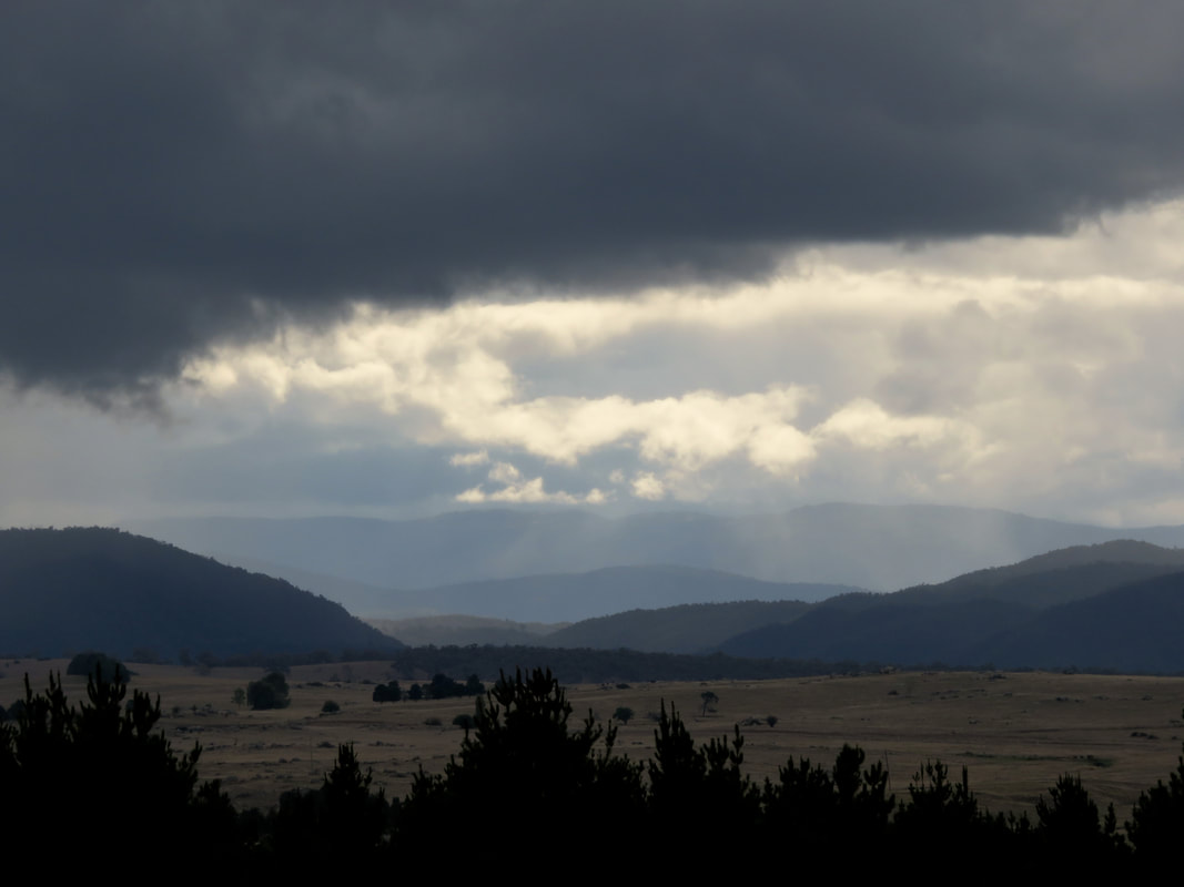 Heavy clouds over wooded hills and dry paddocks