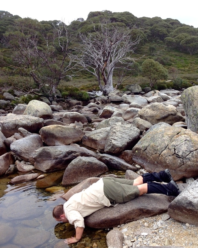 Person lying on rock to drink from stream