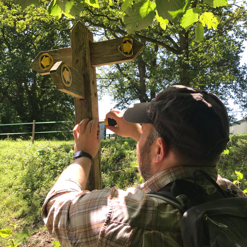 Person in a cap screwing a waymarker into a fingerpost