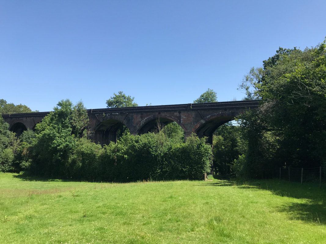 A low brick viaduct with several arches over green field under blue sky